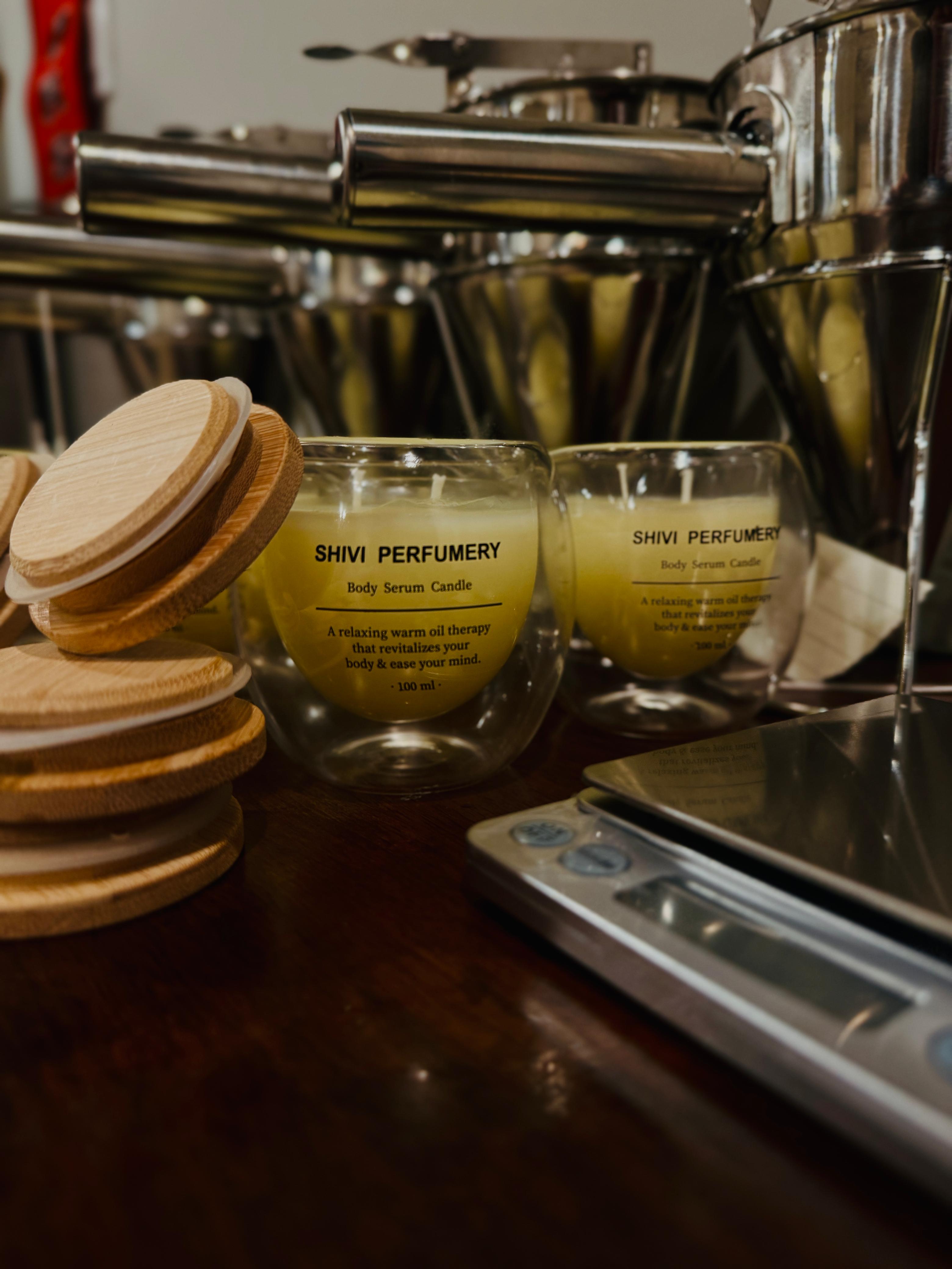 Two glass containers with yellow liquid labeled 'Shivi Perfumery' on a counter with an espresso machine in the background.